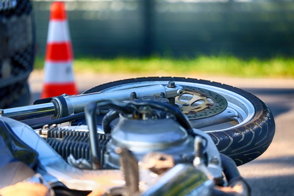 Close-up of a fallen motorcycle wheel on the road with an orange and white traffic cone in the background.