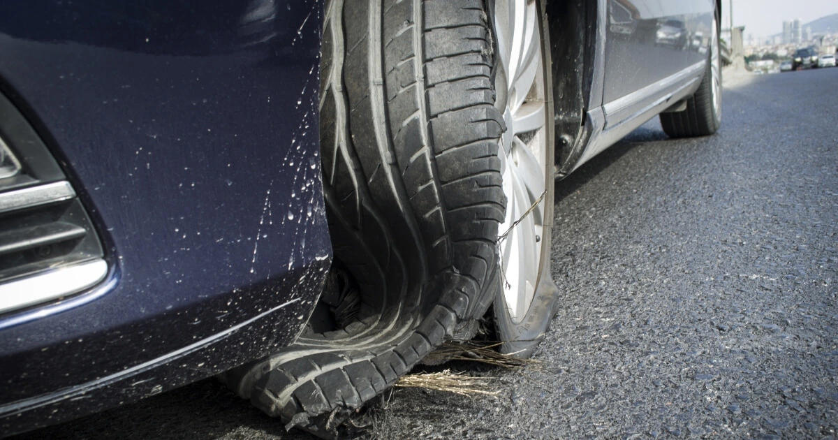 A blue car with a tire blowout on the front wheels on the road.